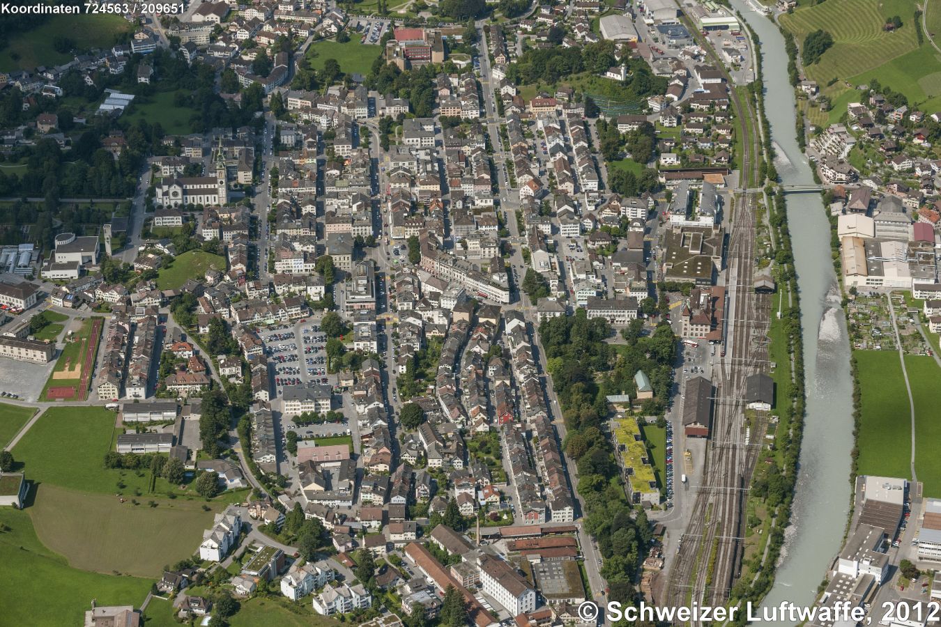 Glarus (Position:2'723'810.87, 1'211'184.63), Links oben im Bild: evangel.-reform. Stadtkirche, ganz links Bildmitte: kathol. Fridolinskirche. Oben im Bild: 'Burghügel Bürgli'. Die Burgstrasse durchquert das Bild, am Strassenende: Kantonsschule. Rechts der Linth: Indstrieareal 'Ennetbühls'